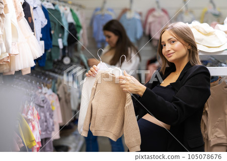 Two pregnant friends shopping together in clothes store. Mothers doing shopping in baby shop. Baby clothes sale and pregnancy concept. Two pregnant friends shopping together in clothes store. Mothers doing shopping in baby shop. Baby clothes sale and pregnancy concept. 105078676