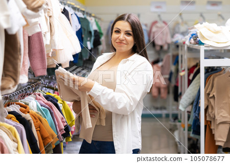 Pregnant woman choosing dress and bodysuits at clothing store. Mother doing shopping in baby shop. Baby clothes sale and pregnancy concept. Pregnant woman choosing dress and bodysuits at clothing store. Mother doing shopping in baby shop. Baby clothes sale and pregnancy concept. 105078677