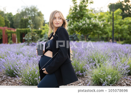 Pregnant woman walking in a park and drinking coffee outdoors. 105078696