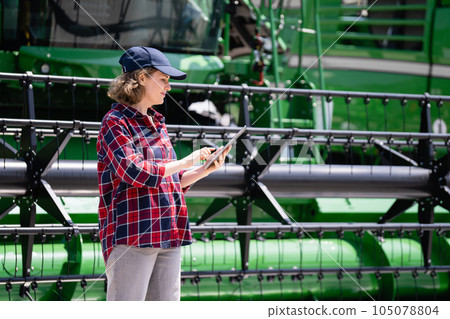 Woman farmer with digital tablet on a background of harvester.  105078804
