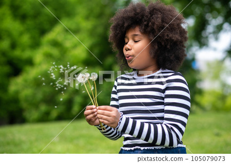 Curly-haired kid blowing on a dandelion Curly-haired kid blowing on a dandelion 105079073