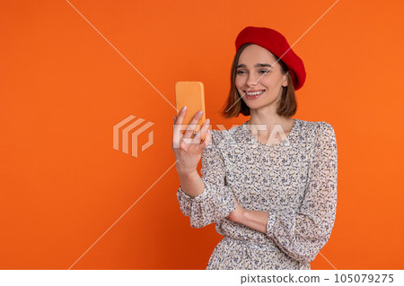 Attractive adult woman wearing elegant dress and red beret making selfie on cell phone. Attractive adult woman wearing elegant dress and red beret making selfie on cell phone. 105079275