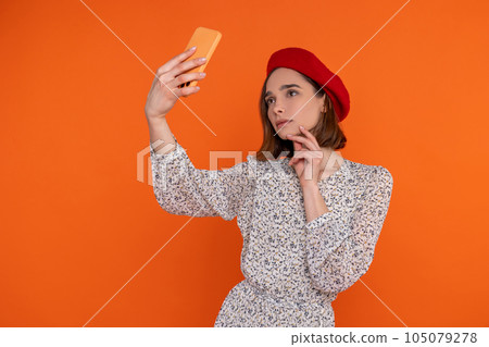Pensive adult woman wearing elegant dress and red beret making selfie on cell phone. Pensive adult woman wearing elegant dress and red beret making selfie on cell phone. 105079278