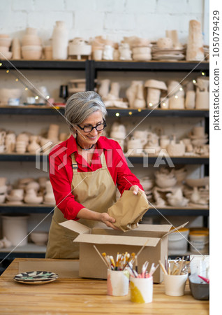 Woman seller or worker of earthenware shop packing order of client and wrapping it into paper. 105079429