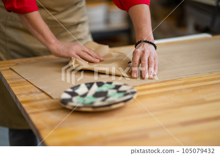 Hands of woman pottery master wrapping earthenware item ordered by client into paper. 105079432