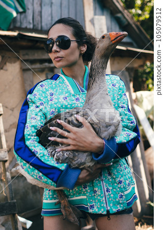Stylish young woman farmer holds goose. 105079512