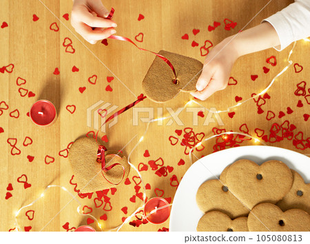 Childs hands making a garland from the selfmade baked heart cookies. Childs hands making a garland from the selfmade baked heart cookies. 105080813