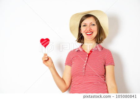 Beautiful girl in summer hat on white background with heart lollipop in her hand for Valentines Day. Beautiful girl in summer hat on white background with heart lollipop in her hand for Valentines Day. 105080841