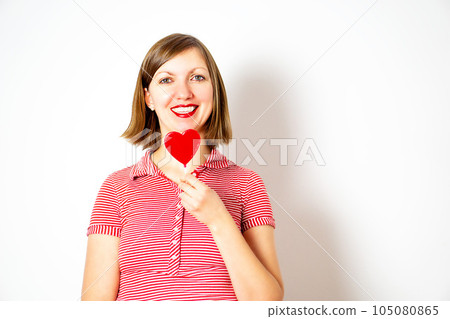 Portrait of the young woman on a white background with a red heart lollipop in her hand. Portrait of the young woman on a white background with a red heart lollipop in her hand. 105080865