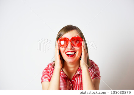 Valentines Day portrait of pretty smiling woman in red sunglasses on the white background. Valentines Day portrait of pretty smiling woman in red sunglasses on the white background. 105080879