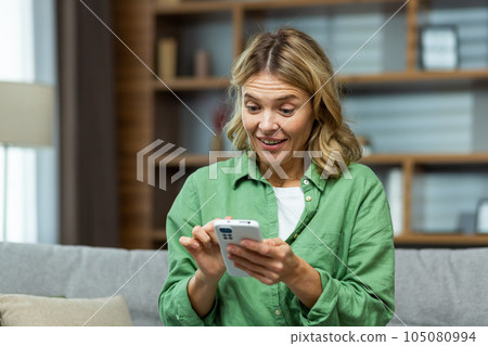 Joyful senior mature woman at home smiling and sitting on sofa, using phone in living room, browsing online pages and dialing message call. Joyful senior mature woman at home smiling and sitting on sofa, using phone in living room, browsing online pages and dialing message call. 105080994