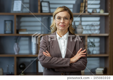 Portrait of serious mature woman inside office at workplace, businesswoman thoughtfully in glasses looking at camera with arms crossed. 105081010