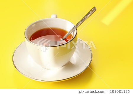 Morning sun shines to white porcelain cup with hot black tea, just brewed, silver spoon in, on yellow board Morning sun shines to white porcelain cup with hot black tea, just brewed, silver spoon in, on yellow board 105081155