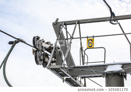 Steel ropes over wheels in mechanism on top of ski chair lift support pillar, number 6 on yellow plate, bright sky background 105081170