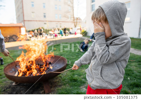 Cute little adorable baby boy put big wooden stick in fire pit with huge fire at house garden yard. Child play dangerous game with bonfire. Fire accident risk and health damgae concept Cute little adorable baby boy put big wooden stick in fire pit with huge fire at house garden yard. Child play dangerous game with bonfire. Fire accident risk and health damgae concept 105081375