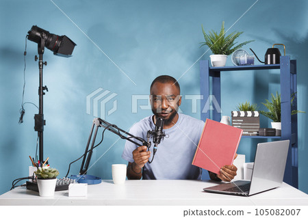 Smiling streamer presenting new book with red cover mockup and looking at camera while live broadcasting for blog. Vlogger recording novel review video for internet podcast 105082007