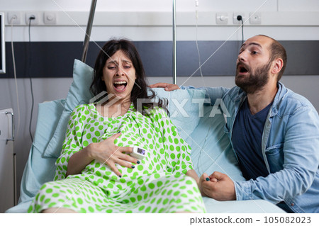 Pregnant woman having painful contractions, getting into labor in hospital ward while nervous husband yelling for doctor and medical assistance. Caucasian young couple preparing for childbirth Pregnant woman having painful contractions, getting into labor in hospital ward while nervous husband yelling for doctor and medical assistance. Caucasian young couple preparing for childbirth 105082023