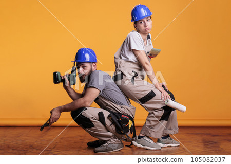 Interior constructors acting confident with building tools, posing on studio background with construction instruments. Holding power drill gun, pair of pliers and painting brushes. 105082037