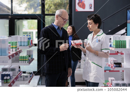 Elderly man buying supplements and getting heart health advice from pharmacist in drugstore. Pharmaceutical specialist explaining senior person differences between vitamin complex Elderly man buying supplements and getting heart health advice from pharmacist in drugstore. Pharmaceutical specialist explaining senior person differences between vitamin complex 105082044