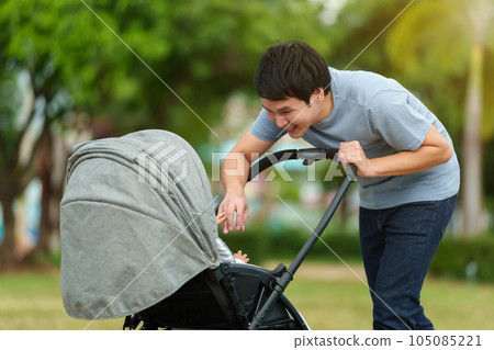 happy father talking and playing with infant baby in the stroller while resting in the park happy father talking and playing with infant baby in the stroller while resting in the park 105085221