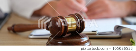 Wooden gavel of judge on table close-up, and blurred doctor doing paperwork in medical clinic. Wooden gavel of judge on table close-up, and blurred doctor doing paperwork in medical clinic. 105086533