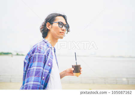A man walking along the beach with take-out coffee 105087162