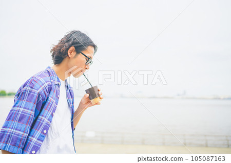A man walking along the beach with take-out coffee 105087163