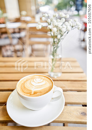 Cup of hot cappuccino. The table in the coworking space of the coffee shop. A cup of coffee on the veranda on a sunny day. Coffee break at the cafe. Close-up 105087606