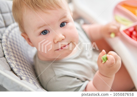 Cute child eats healthy food pasta and vegetables steamed,. Portraits of a cute 10 months old baby girl. The baby sitting in a special high chair for babies.  105087658