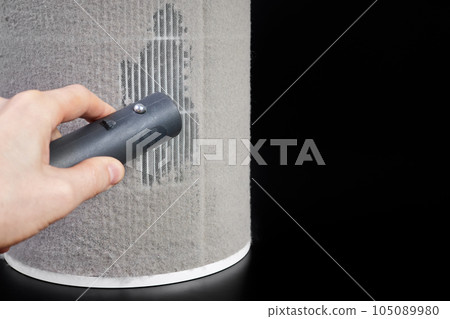 A man removes a layer of dust on the filter of a home air purifier using a vacuum cleaner 105089980