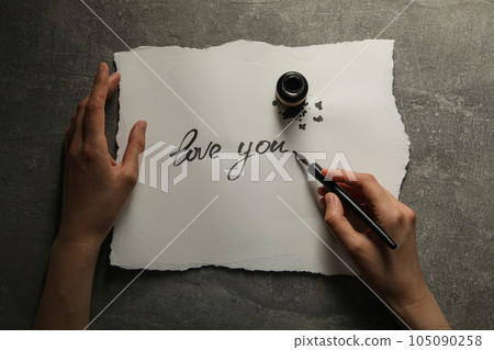 Ink bottle, pen in hand and words Love you on paper on gray background, top view Ink bottle, pen in hand and words Love you on paper on gray background, top view 105090258