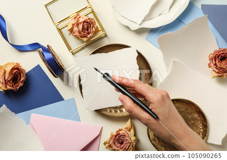 Pieces of paper, roses, golden plates and pen in hand on white background, top view Pieces of paper, roses, golden plates and pen in hand on white background, top view 105090265