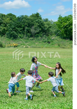 Children and women playing in a circle on a meadow 105090599