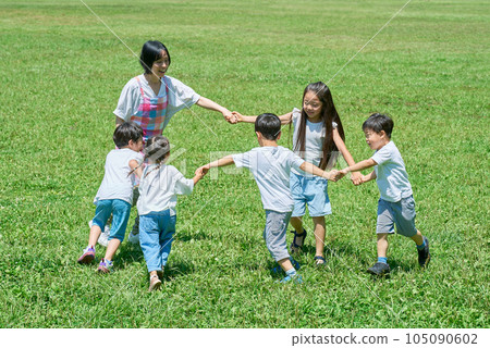 Children and women playing in a circle on a meadow 105090602