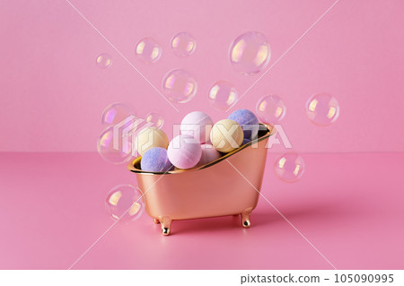 Salt bath bombs in a bathtub with soap bubbles on pink background. Creative idea of bath bombs, body care beauty treatment. Salt bath bombs in a bathtub with soap bubbles on pink background. Creative idea of bath bombs, body care beauty treatment. 105090995