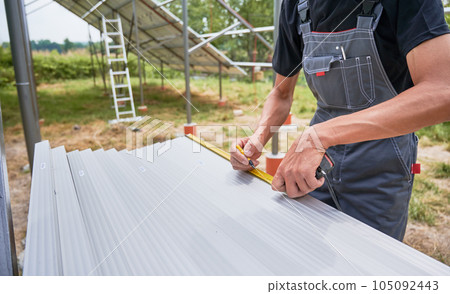 Worker measuring metal beams with measuring tape for installing solar panels. Renewable and ecological energy. Environment safe. Modern technology and innovation. Cropped image of man in workwear 105092443