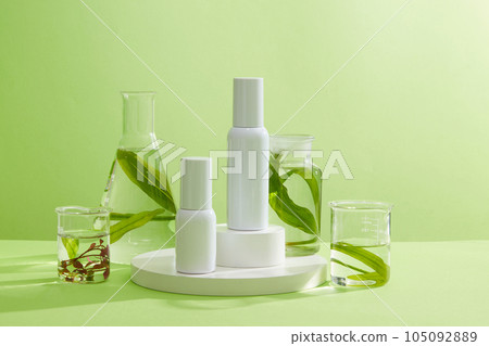 Front view of two cosmetic bottles on round podiums decorated with glass jars containing marine plant samples on pastel green background. Mockup scene for advertising cosmetic of seaweed extract. Front view of two cosmetic bottles on round podiums decorated with glass jars containing marine plant samples on pastel green background. Mockup scene for advertising cosmetic of seaweed extract. 105092889