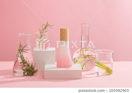 Minimalist empty display product presentation scene. Cosmetic bottle unbranded on white podiums decorated with experimental flasks filled with seaweed and transparent liquid on pink background Minimalist empty display product presentation scene. Cosmetic bottle unbranded on white podiums decorated with experimental flasks filled with seaweed and transparent liquid on pink background 105092903