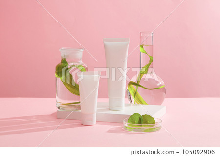 Mockup scene for advertising cosmetic with natural extract. Two plastic bottle unbranded decorated with lab glassware filled with seaweed and centella leaves on a pink background. Mockup scene for advertising cosmetic with natural extract. Two plastic bottle unbranded decorated with lab glassware filled with seaweed and centella leaves on a pink background. 105092906
