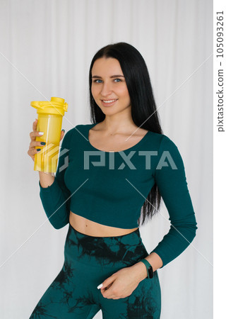 Athletic young woman holding a bottle of water after a workout at home Athletic young woman holding a bottle of water after a workout at home 105093261