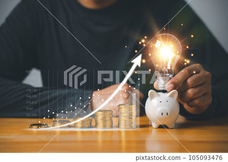 Saving money with a lightbulb concept. Hand holding a light bulb with a coins stack and chart graph, representing financial planning for the future. This creative concept is a symbol of success. 105093476