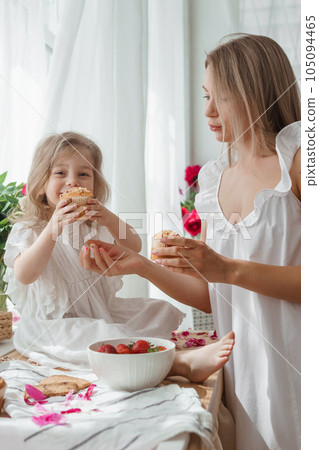 A little blonde girl with her mom on a kitchen countertop decorated with peonies. The concept of the relationship between mother and daughter. Spring atmosphere. A little blonde girl with her mom on a kitchen countertop decorated with peonies. The concept of the relationship between mother and daughter. Spring atmosphere. 105094465