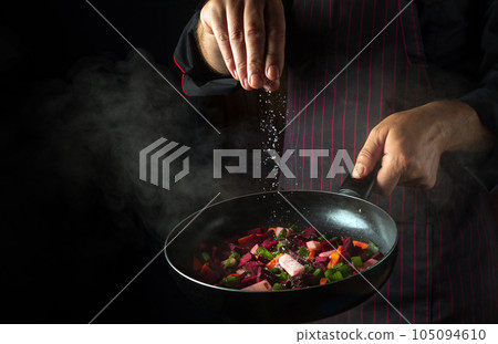 Cooking fresh vegetables. Chef adds salt to a steaming hot pan. The idea of European cuisine for a hotel with advertising space 105094610