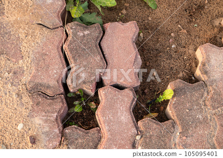 A crumbling red cobblestone road. Gravel and green grass A crumbling red cobblestone road. Gravel and green grass 105095401