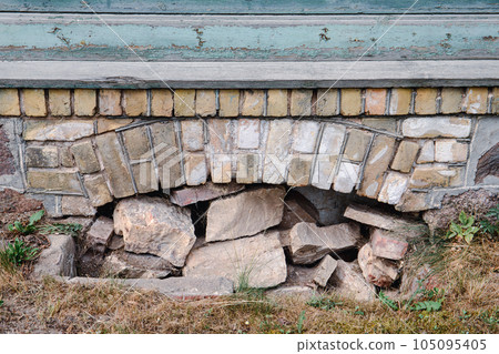 The basement window of an old stone and brick house filled with stones. History and construction 105095405