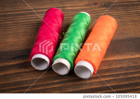 Colorful threads in spools on a wooden texture background Colorful threads in spools on a wooden texture background 105095418