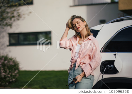 Young woman charging her electric car in home, sustainable and economic transportation concept. Young woman charging her electric car in home, sustainable and economic transportation concept. 105096268