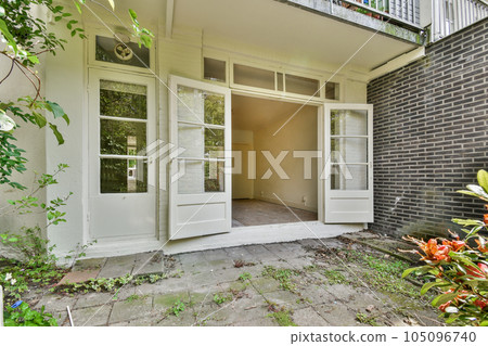 the outside of a house with an open door and some plants growing in the front yard, on a sunny day 105096740