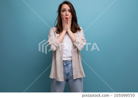 upset surprised young brunette female adult in casual shirt on blue background 105099550