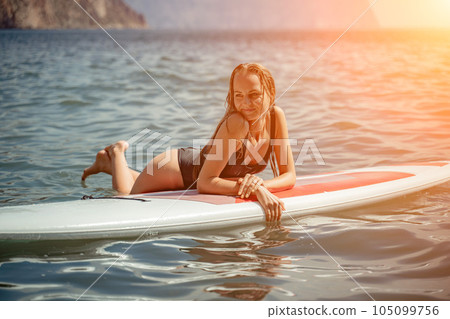 Woman sup sea. Sports girl on a surfboard in the sea on a sunny summer day. In a black bathing suit, he sits on a sapa in the sea. Rest on the sea. 105099756